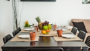 Een eettafel gedekt met borden, bestek en een schaal fruit.