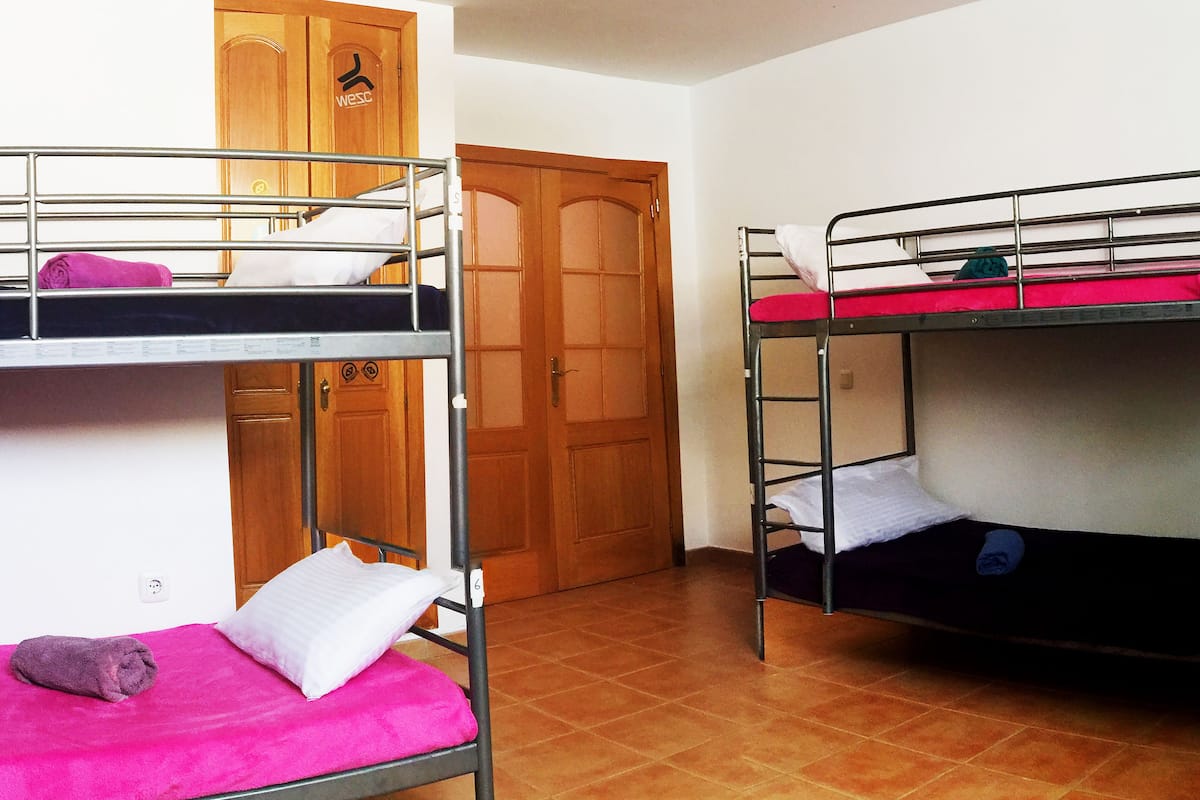 Une chambre de dortoir avec des lits superposés, une armoire en bois et un plafonnier blanc.