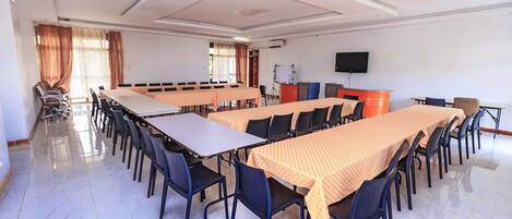 A conference room with multiple tables and chairs, a whiteboard, and a television on the wall.