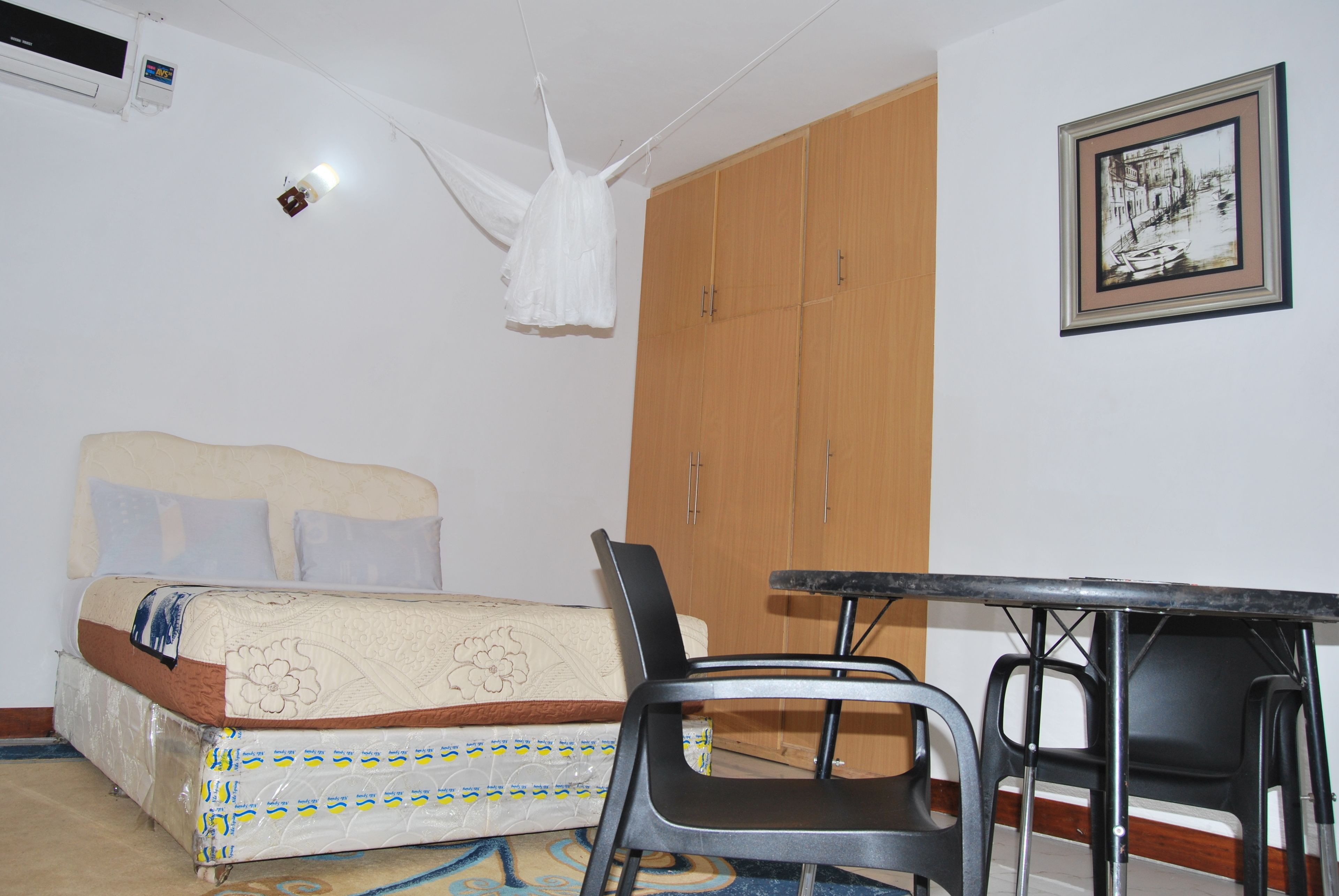 A bedroom with a bed, a wooden wardrobe, a framed picture on the wall, and a table with chairs.