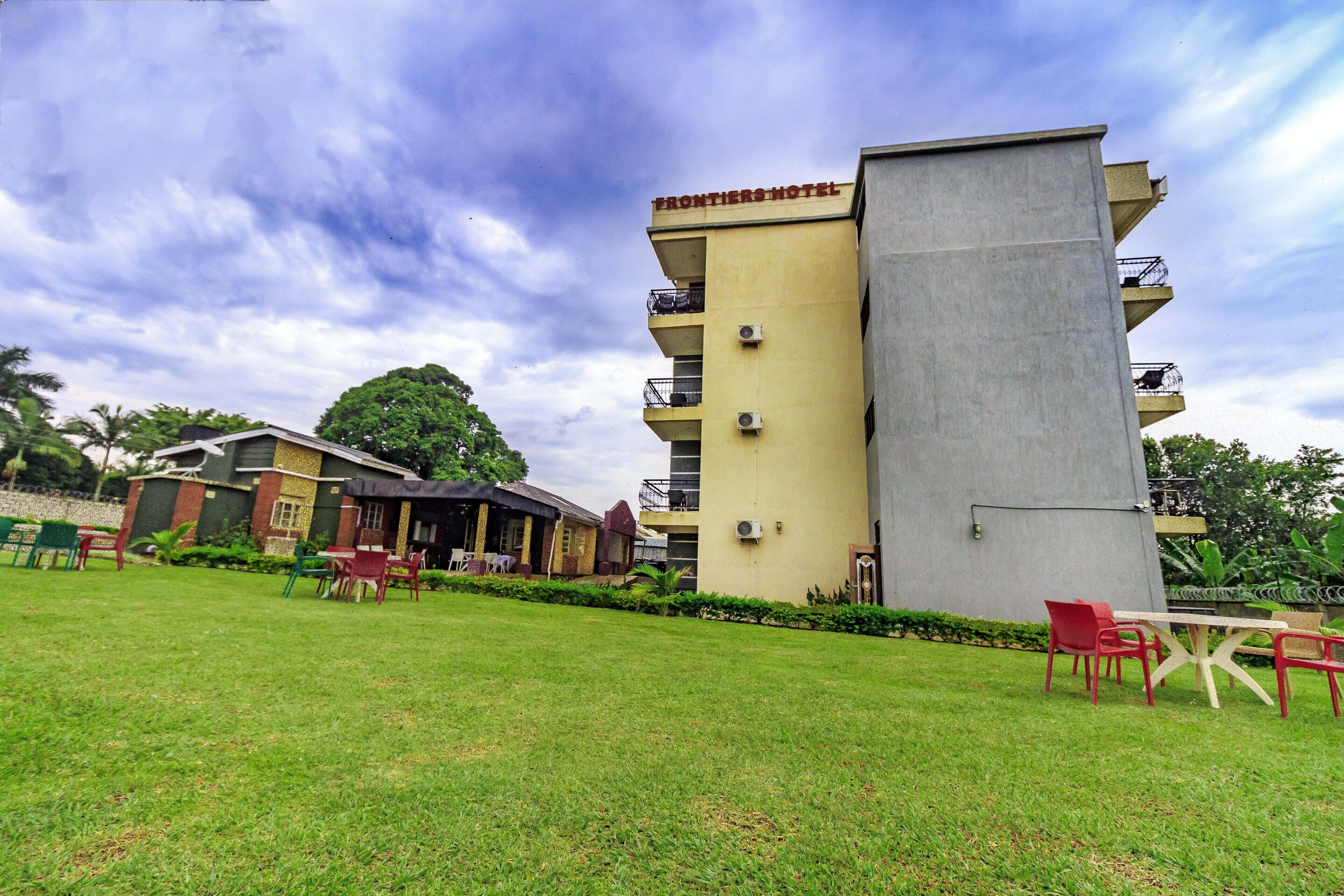 A hotel with a flat roof, multiple balconies, and a well-maintained lawn with outdoor seating.