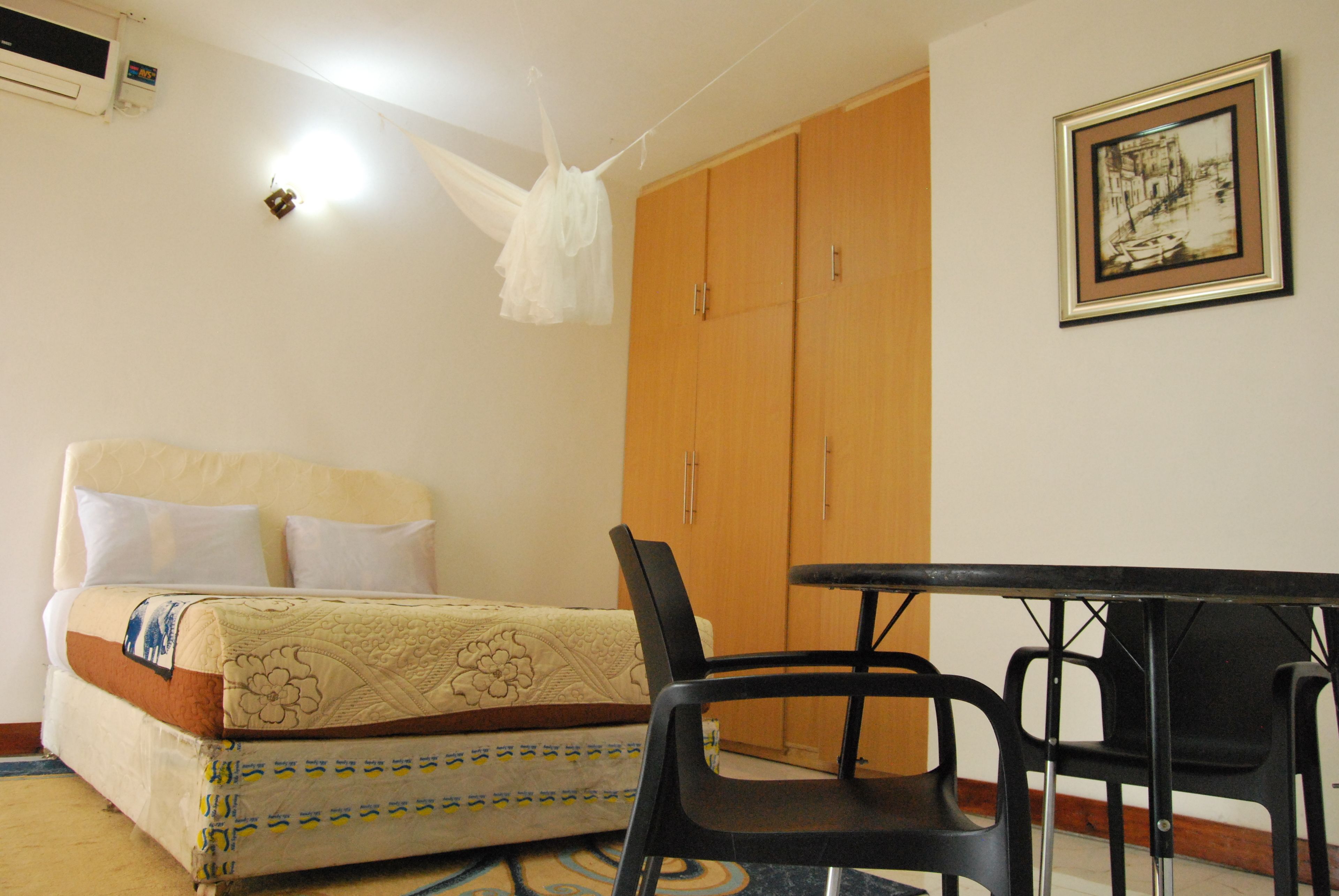 A bedroom with a bed, a wooden wardrobe, a table with chairs, and a hanging light fixture.