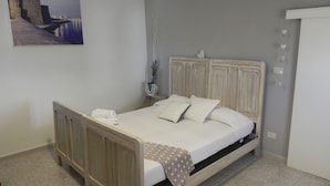 Quarto com cama de madeira, mesa de cabeceira, luminária de parede e quadro emoldurado.