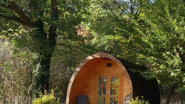 Eine Holzhütte mit gewölbtem Dach, einem Picknicktisch und einem Stuhl davor.