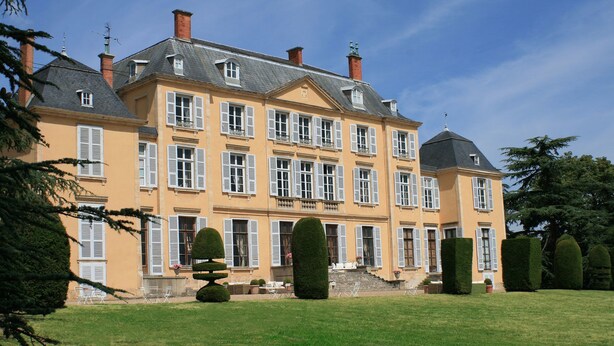 A large, multi-story building with symmetrical architecture, featuring numerous windows with shutters, a well-maintained lawn, and neatly trimmed hedges. - Château de Saint Trys (Anse)