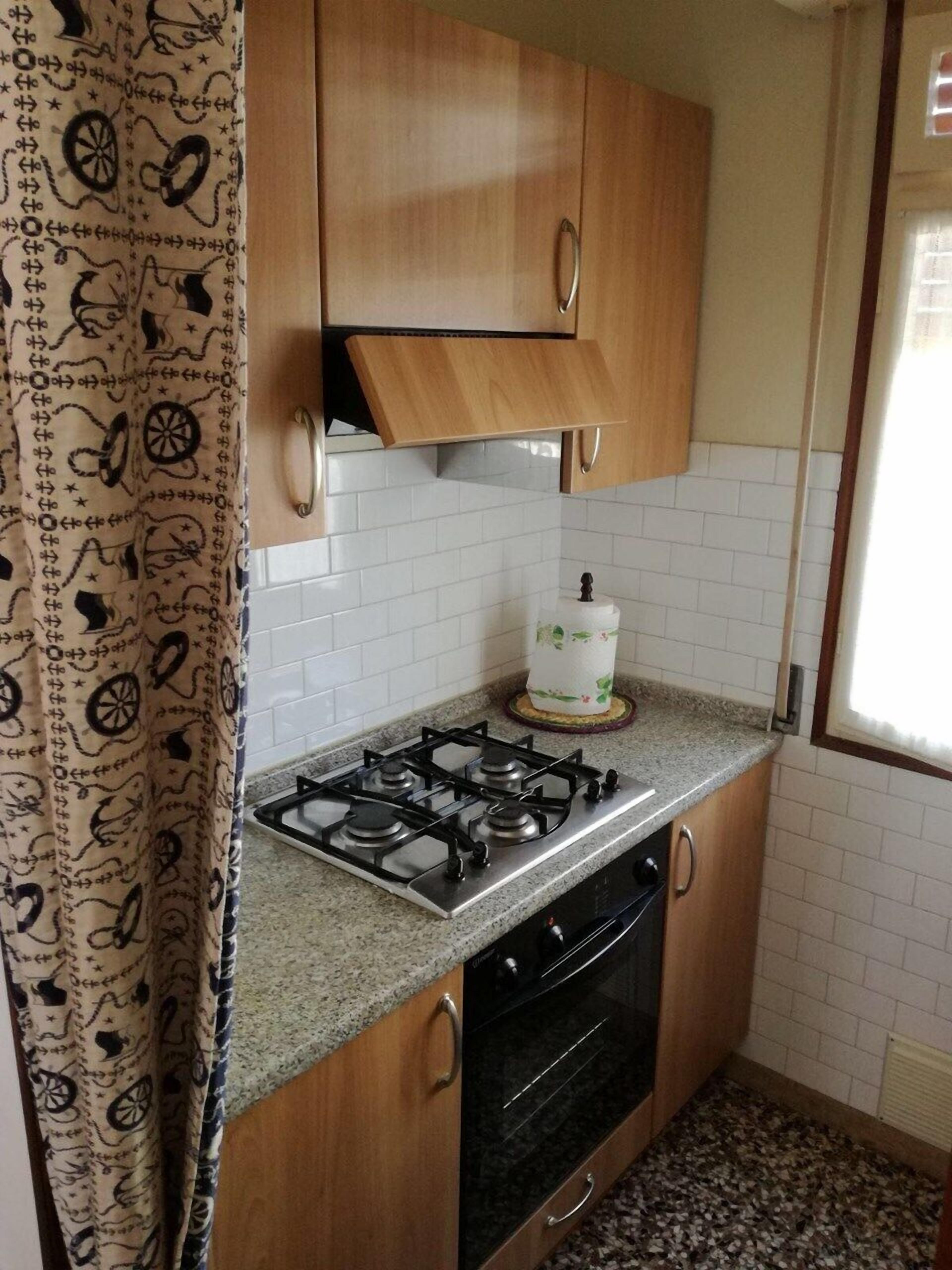 A kitchen with wooden cabinets, a gas stove, an oven, and a window with blinds.