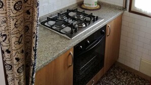 A kitchen with wooden cabinets, a gas stove, an oven, and a window with blinds. - Villa Dilva (San Michele al Tagliamento)