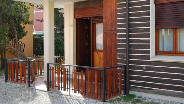 A modern building with a wooden facade, a balcony with a metal railing, and a staircase leading to an upper level. - Villa Dilva (San Michele al Tagliamento)