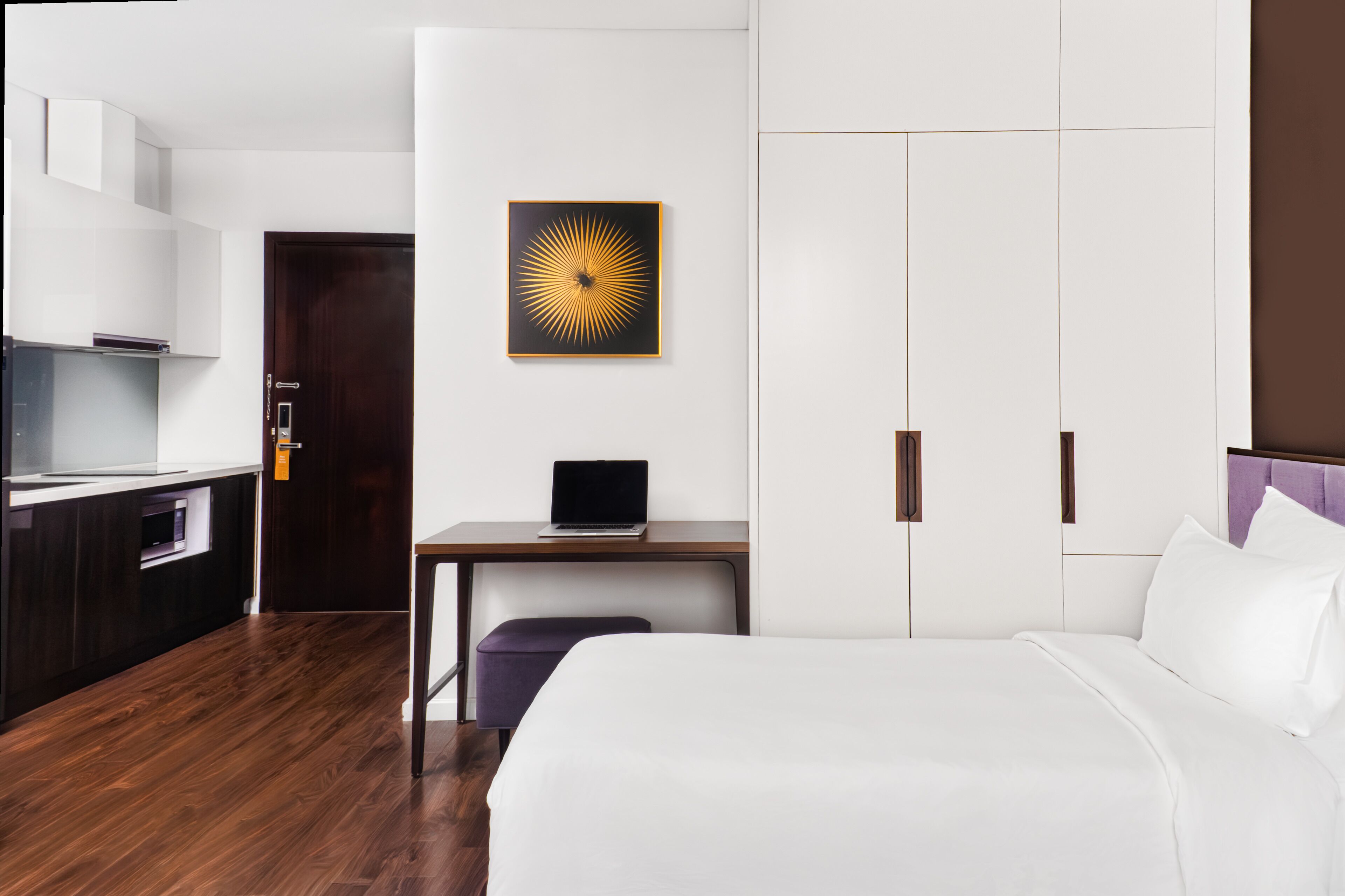 Ein Hotelzimmer mit Bett, Schreibtisch mit Laptop, Kleiderschrank und einer Küchenzeile.