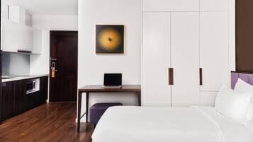 Ein Hotelzimmer mit Bett, Schreibtisch mit Laptop, Kleiderschrank und einer Küchenzeile.