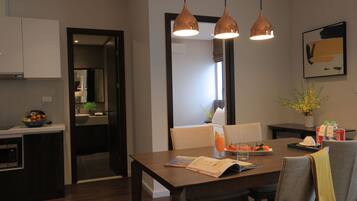 A modern dining area with a wooden table, two pendant lights, and a view into the kitchen.