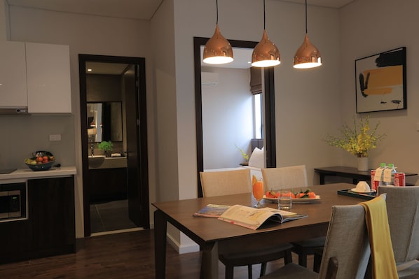 A modern dining area with a wooden table, two pendant lights, and a view into the kitchen. - Mandala Hotel and Spa (Vu Ninh)