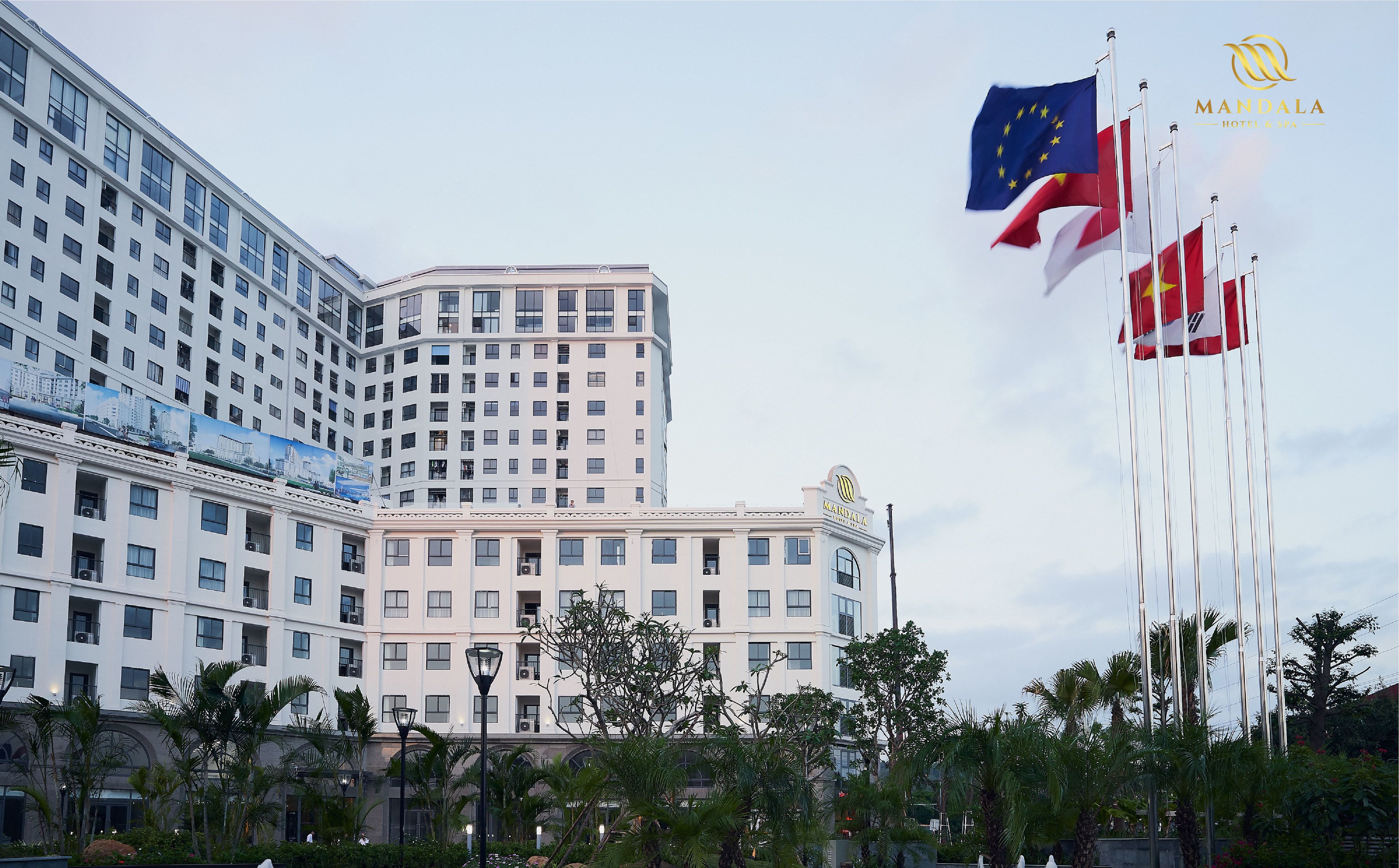 Een hotel met meerdere vlaggen, waaronder de vlag van de Europese Unie, en een opvallend logo van Mandala Hotel & Spa.