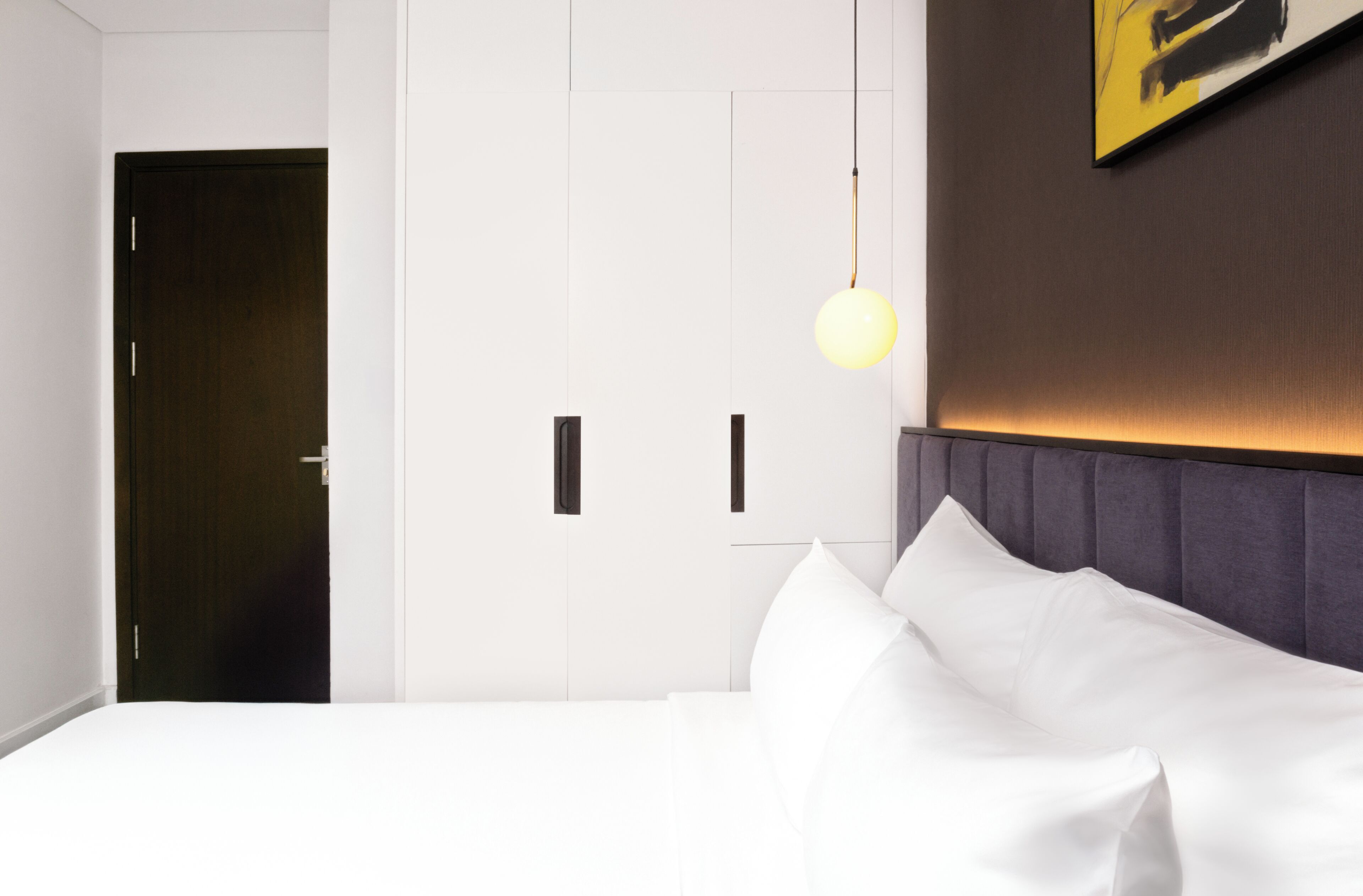 A hotel room with a bed, a wardrobe, and a hanging light fixture.
