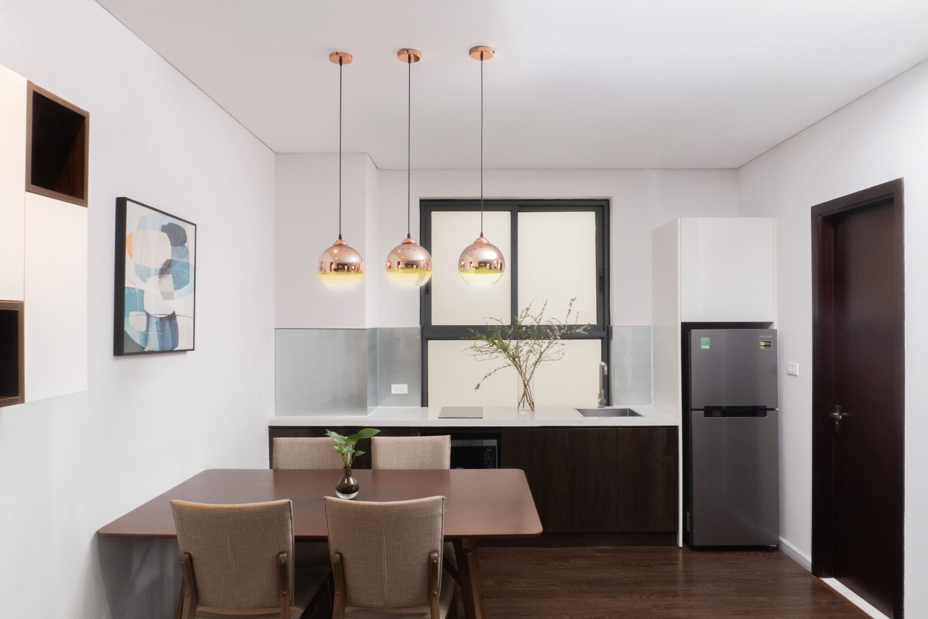 Eine moderne Küche mit Esstisch, Stühlen, Pendelleuchten, einem Kühlschrank und einem Fenster mit Blick.