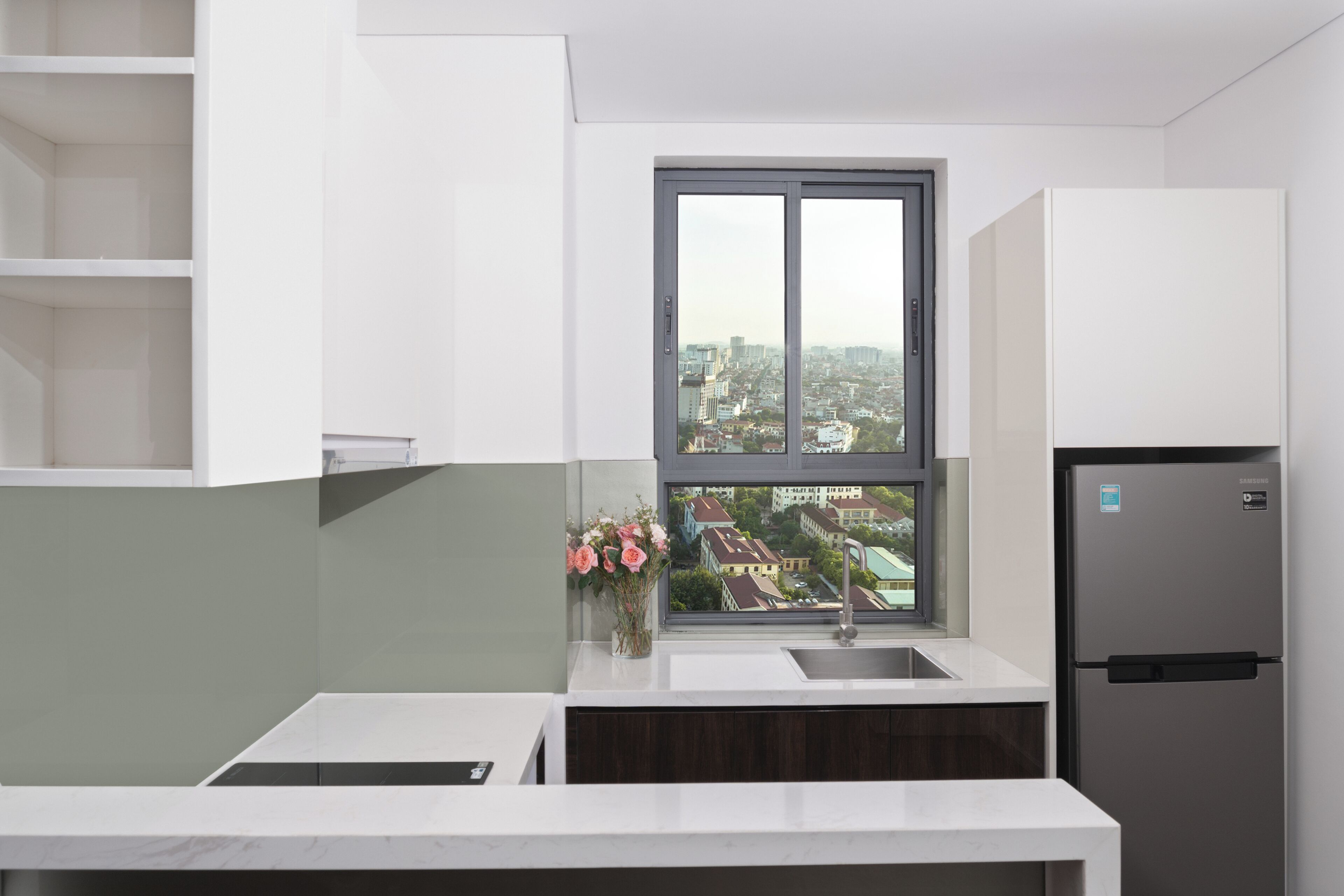 A modern kitchen with a built-in refrigerator, a window with a view of a cityscape, and a vase with flowers on the counter.