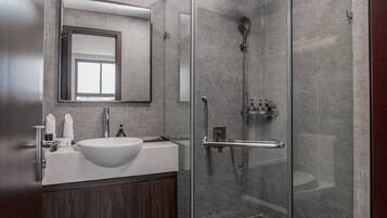 Un bagno moderno con doccia vetrata, un lavandino bianco e uno specchio grande sopra il mobile.