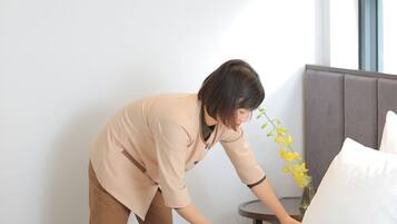 A person adjusting a bed in a room with a window and a plant on a bedside table.