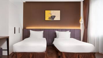 Et hotelværelse med to senge, et skrivebord, en lampe og et maleri på væggen.