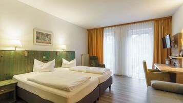 Habitación de hotel con dos camas, un escritorio, una silla, un televisor y un cuadro en la pared.