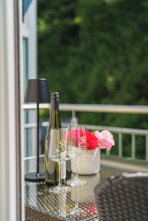 A glass table with a bottle of wine, two wine glasses, a lamp, and a vase with flowers. - Stadthotel Pfeffermuhle (Gengenbach)
