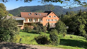 A two-story building with a sloped roof, surrounded by greenery and hills in the background. - Hotel Morgensonne (Badenweiler)