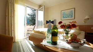 A hotel room with a bed, a table with a bottle of wine, a vase with flowers, and a bowl of fruit. - Hotel Morgensonne (Badenweiler)
