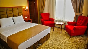 A hotel room with a large bed, two red armchairs, a small wooden table, and a window with curtains. - Aksehir Elitt Hotel (Aksehir)