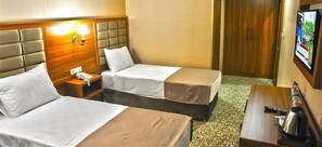Habitación de hotel con dos camas, una mesita de noche con teléfono, un televisor en la pared y una cafetera sobre una mesita auxiliar.