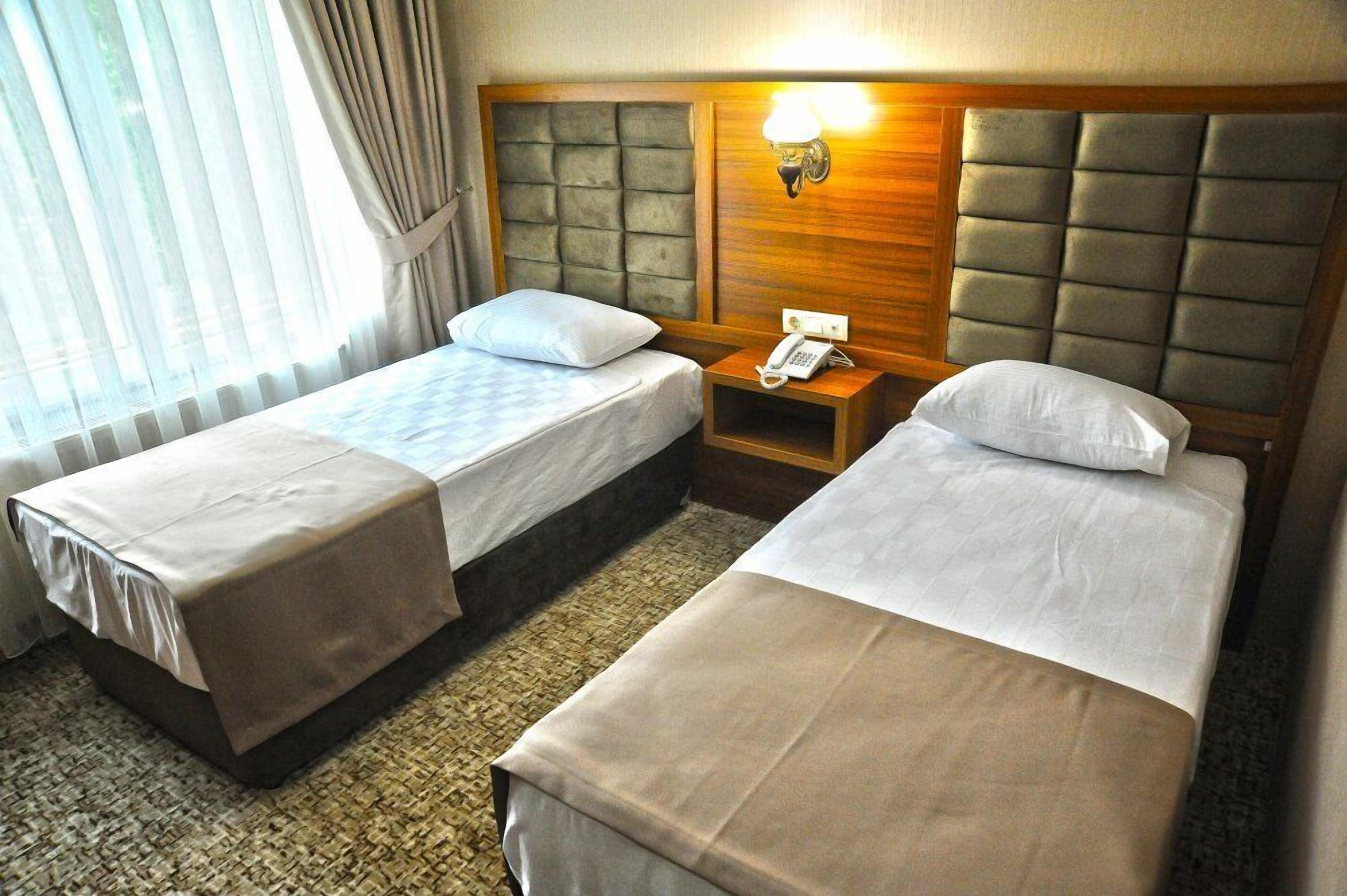 A hotel room with two beds, a wooden headboard, a bedside table with a lamp, and a telephone.