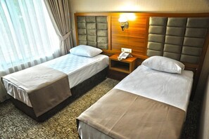 Habitación de hotel con dos camas, cabecera de madera, mesita de noche con lámpara y teléfono.