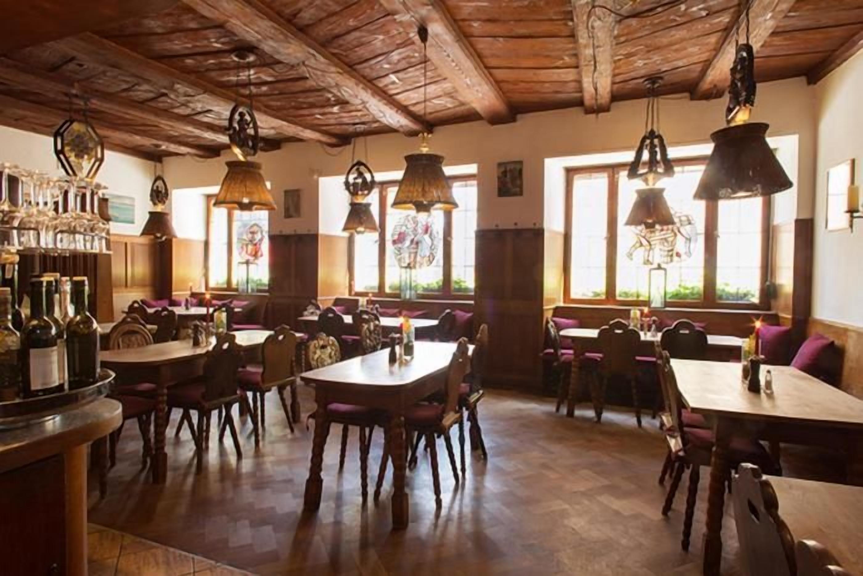 A restaurant with wooden tables and chairs, hanging pendant lights, and a bar area with bottles.