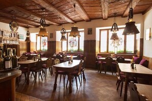 A restaurant with wooden tables and chairs, hanging pendant lights, and a bar area with bottles. - Hotel Residenz (Ravensburg)