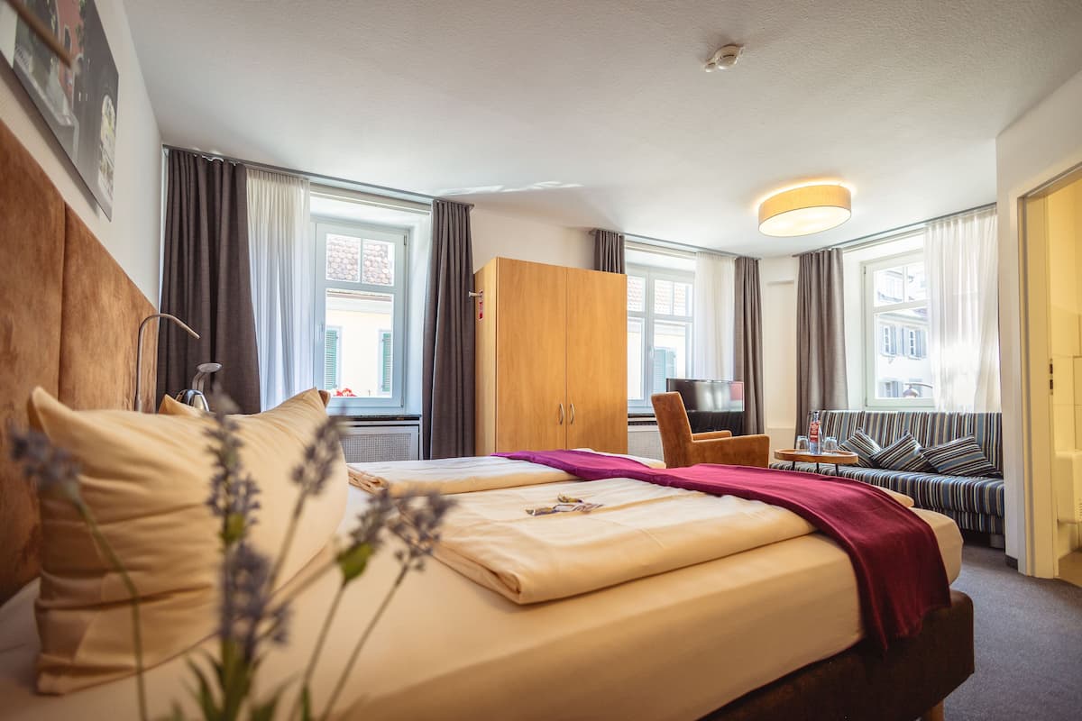 Hotellihuone, jossa on sänky, puinen vaatekaappi, oleskelualue sohvineen ja televisio.