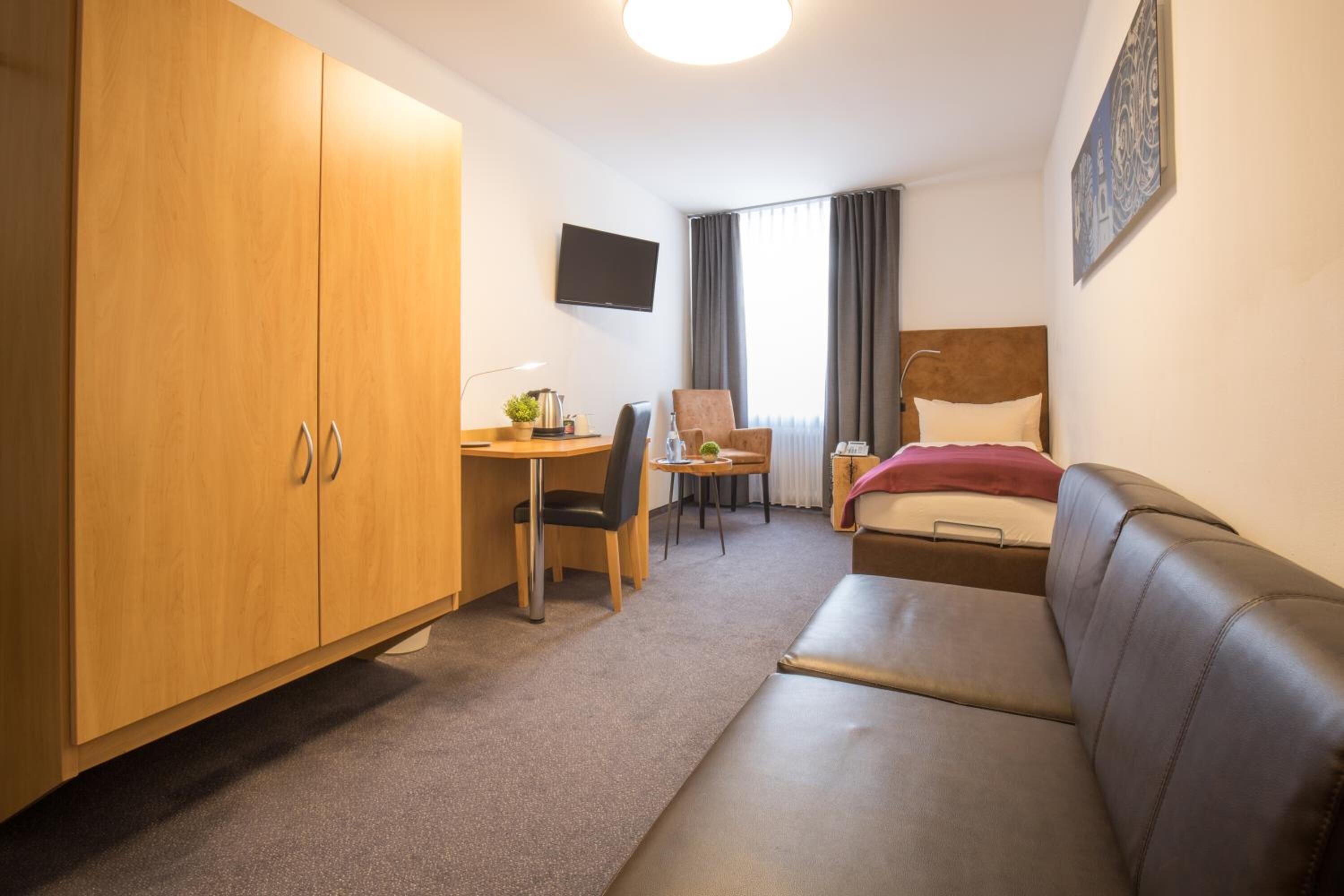 Habitación de hotel con cama, escritorio con silla, armario y televisor en la pared.