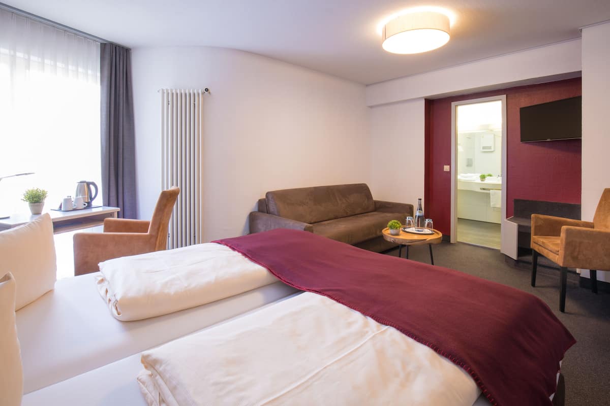 Hotellihuone, jossa on kaksi sänkyä, sohva, pieni pöytä, jossa on kasvi, ja seinälle asennettu televisio.