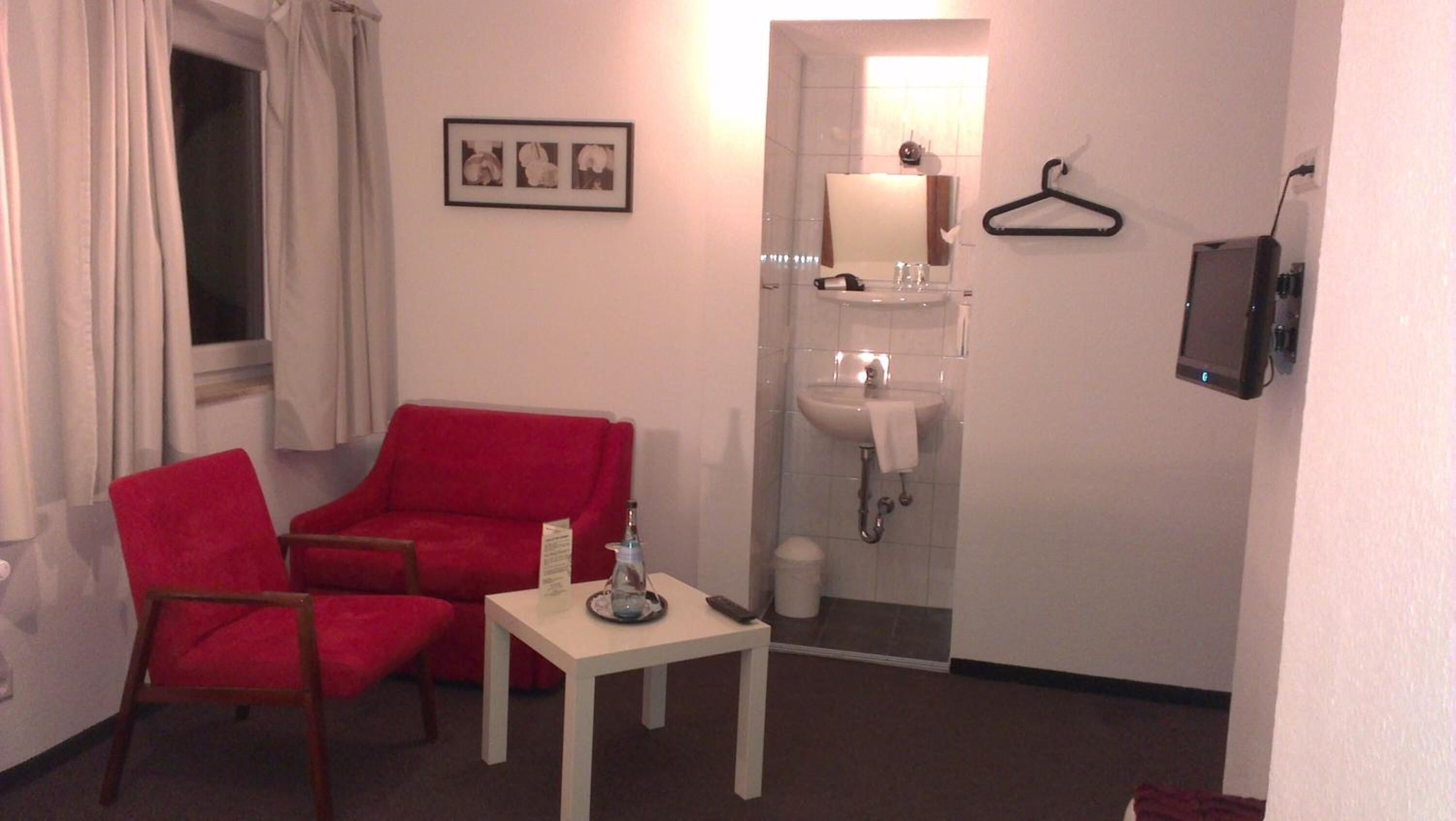A small room with a red chair, a small table, a white sink, and a mirror.