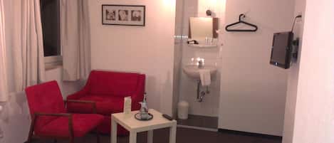 A small room with a red chair, a small table, a white sink, and a mirror.
