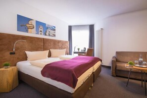 Una habitación de hotel con una cama grande, un sofá, una mesita y una ventana con cortinas.