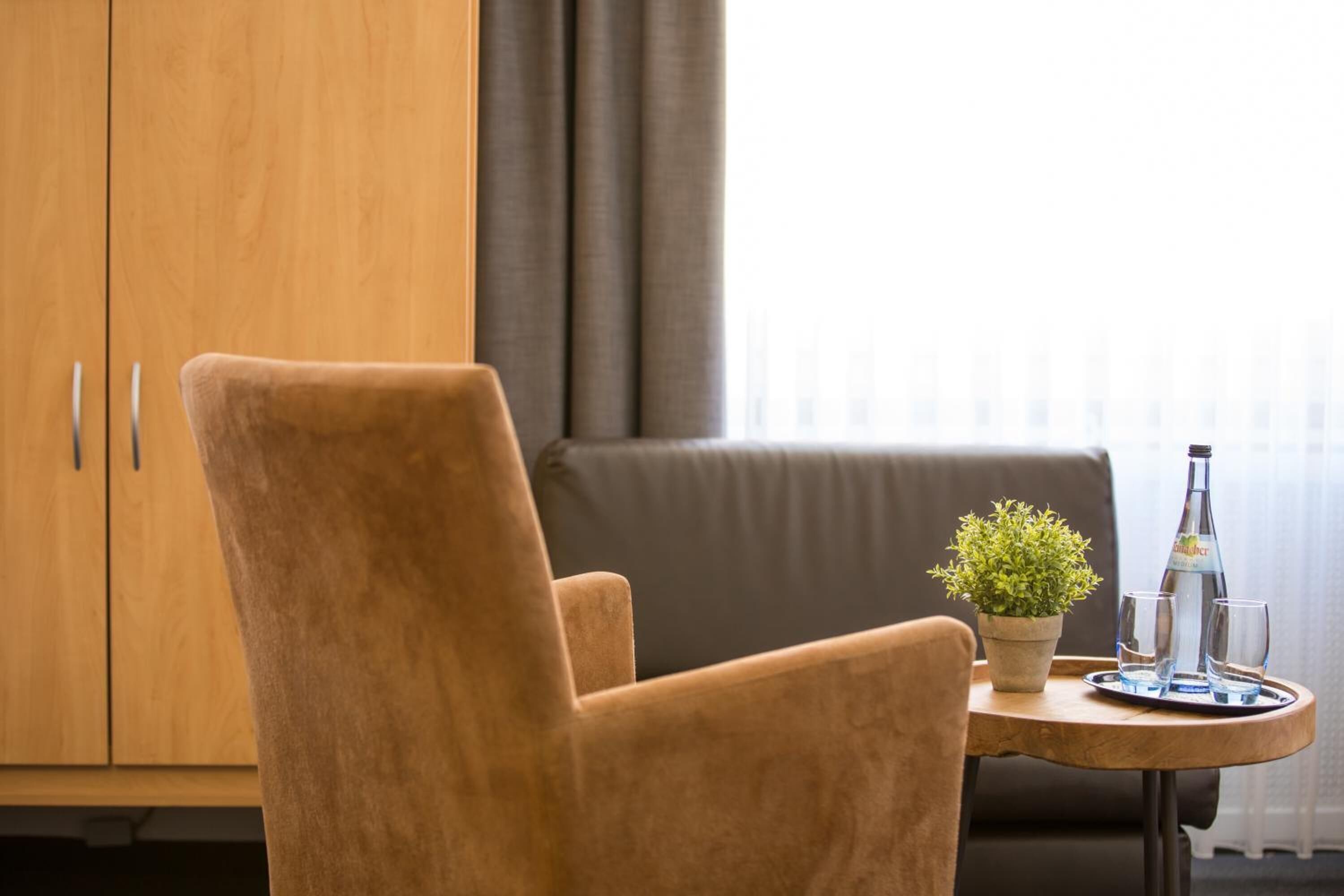 A brown armchair next to a small wooden table with a potted plant, a bottle, and two glasses.