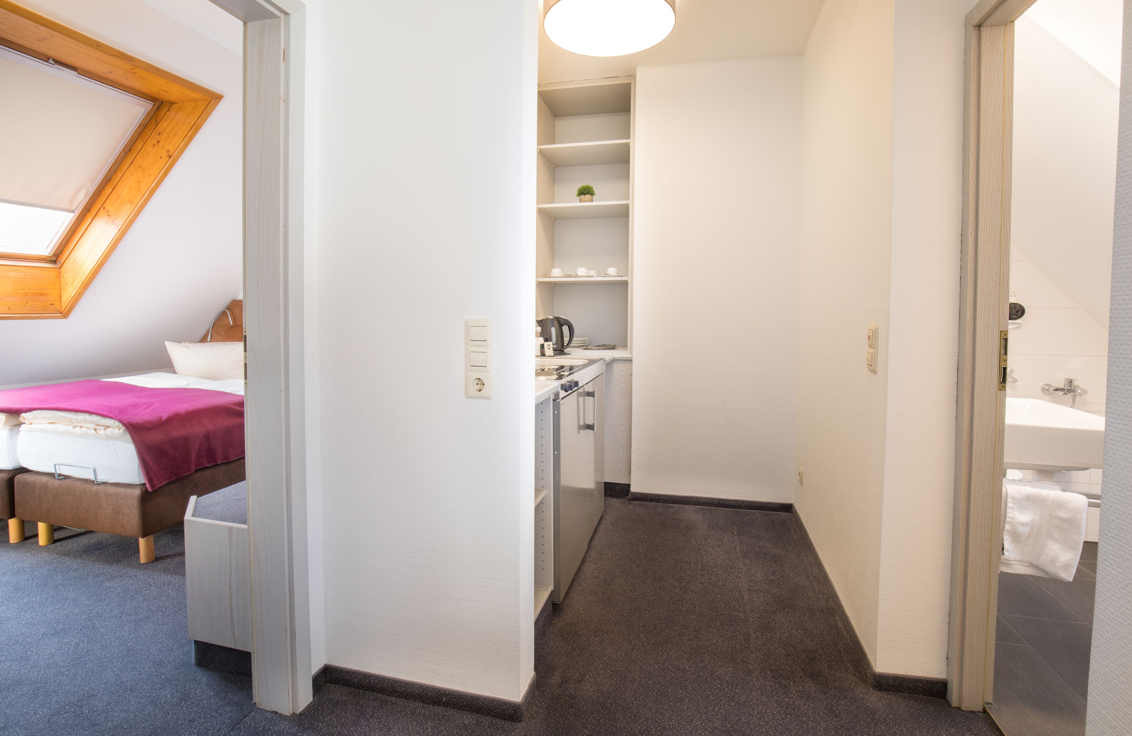Une chambre d’hôtel comprenant un lit, une petite kitchenette, une salle de bain et une lucarne.