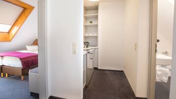 Une chambre d’hôtel comprenant un lit, une petite kitchenette, une salle de bain et une lucarne.