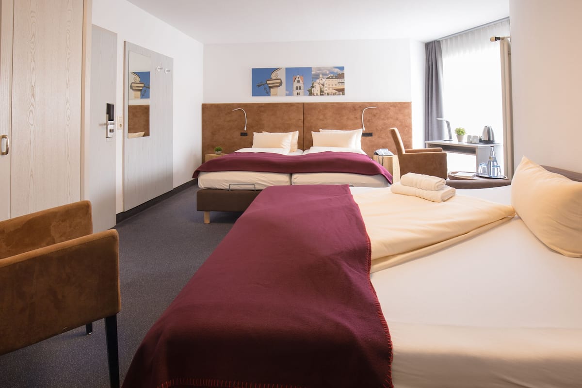 Hotellihuone, jossa on sänky, penkki, työpöytä ja ikkuna, josta on näkymä rakennuksiin.