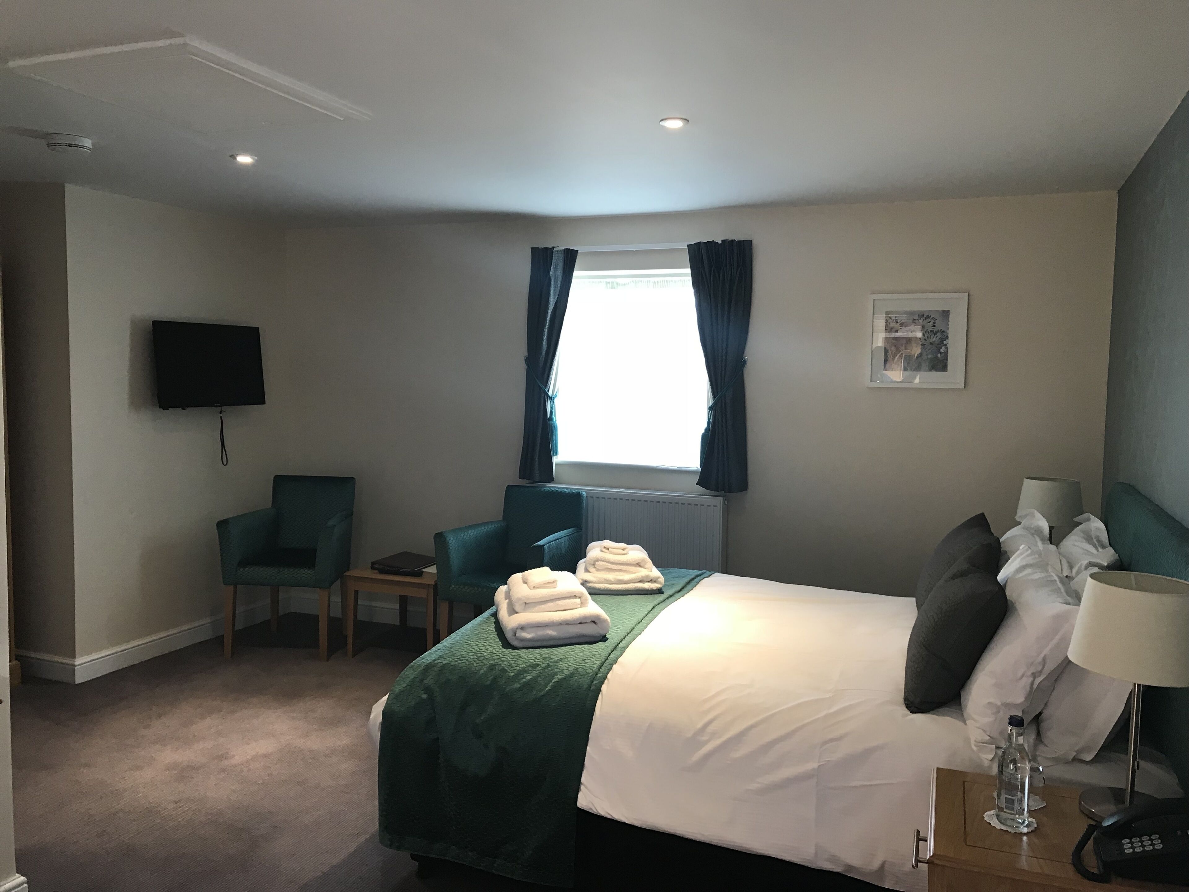 A hotel room with a bed, a desk, a chair, a TV, and a window with curtains.