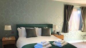 A neatly made bed with a green headboard, two bedside tables with lamps, and a window with curtains.