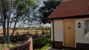 A small building with a brick wall and a wooden door, surrounded by a fence and trees.