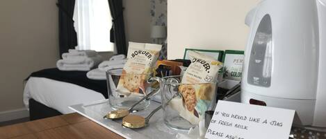 Een hotelkamer met een ontbijttafel, inclusief cornflakes, een melkkannetje en een bordje met daop het aanbod van verse melk aan de bar.