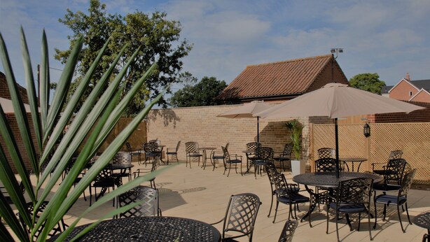 An outdoor patio with round tables and chairs, a large umbrella, and a brick wall.