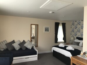 A hotel room with a bed, a sofa, a bedside table with a lamp, a mirror, and a window with curtains.