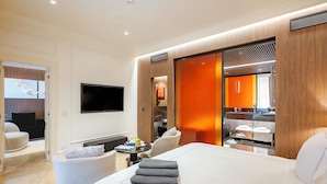 Une chambre d’hôtel moderne dotée d’un grand lit, d’un téléviseur à écran plat, d’un coin salon avec une table et d’une salle de bain visible à travers une porte ouverte.